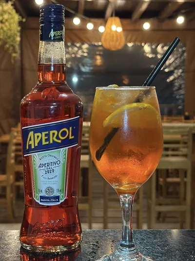 Taça de Aperol Spritz ao lado da garrafa de Aperol