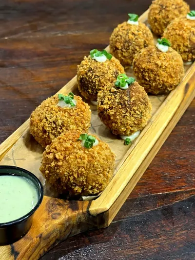 Bolinhos empanados servidos na tábua com molho verde