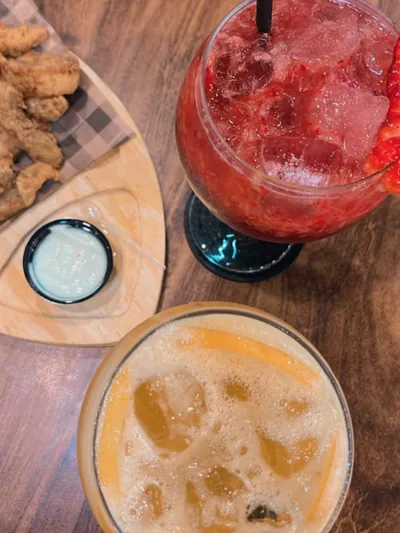 Drinks coloridos e porção de frango vistos de cima na mesa de madeira